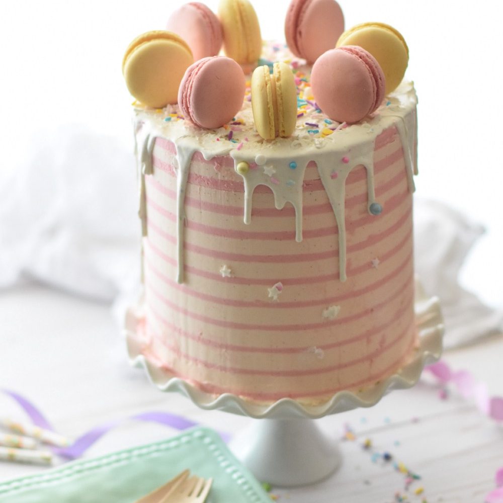 a pastel-colored macaron-topped pink cake on a cake plate.