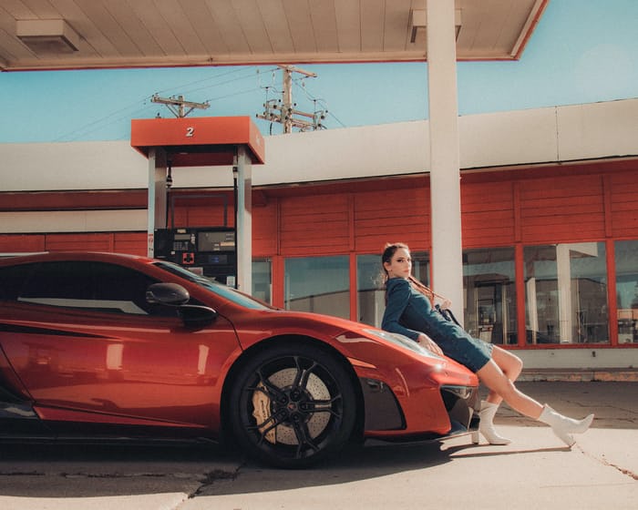 influencer marketing for a red car, model leaning on the car in front of a gas station